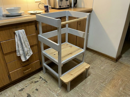 Wooden learning tower in a kitchen setting with wooden cabinets and a tiled floor.